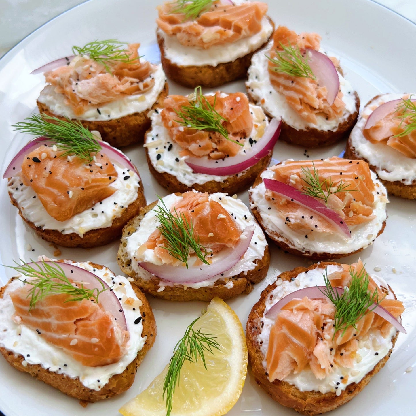 Smoked salmon crostini with cream cheese, onions, and dill on a white plate.