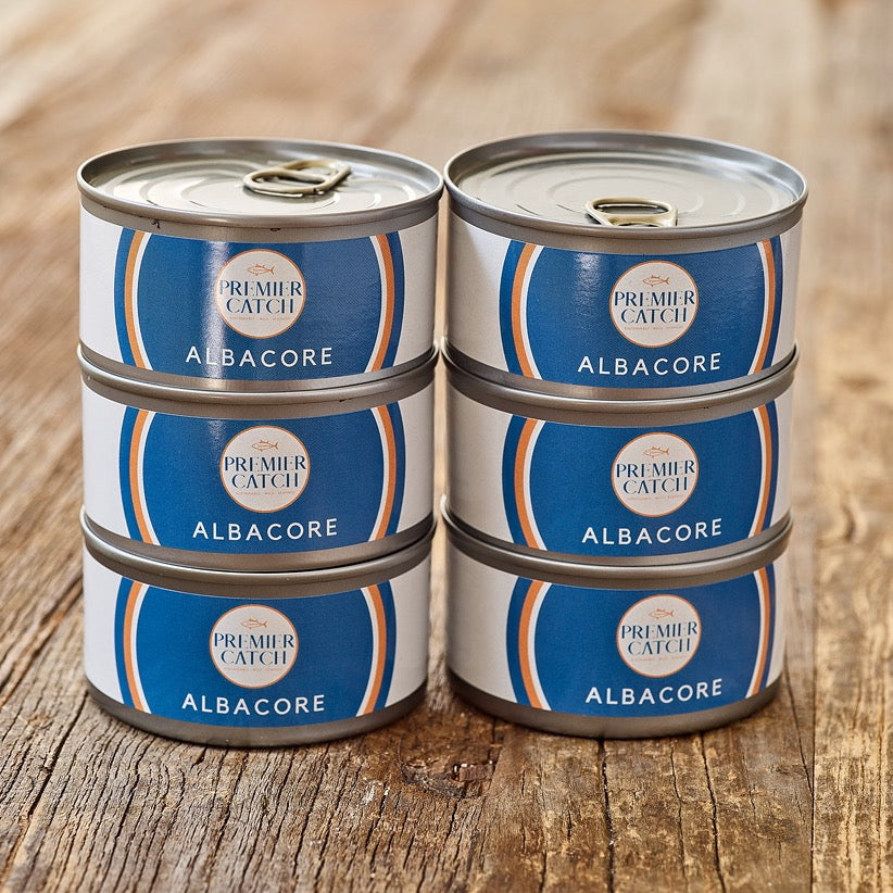 Six pack of wild albacore tuna cans stacked on a wooden surface.