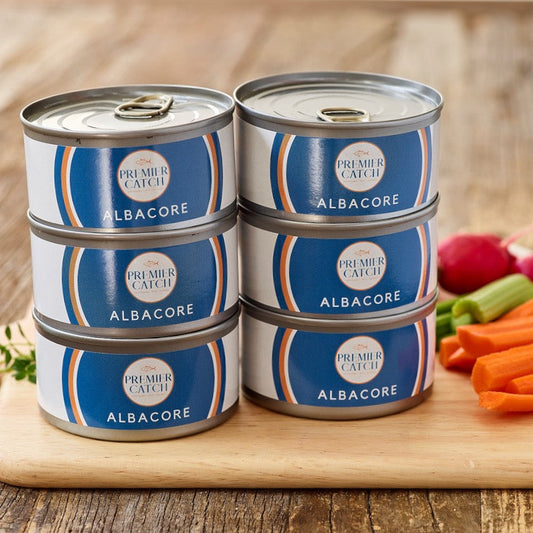 Stack of Premier Catch Albacore tuna cans on a wooden surface with vegetables in the background.