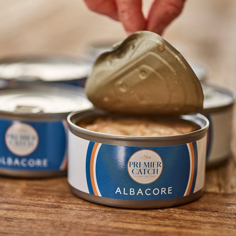 Wild albacore tuna can with pop top lid being opened by hand.