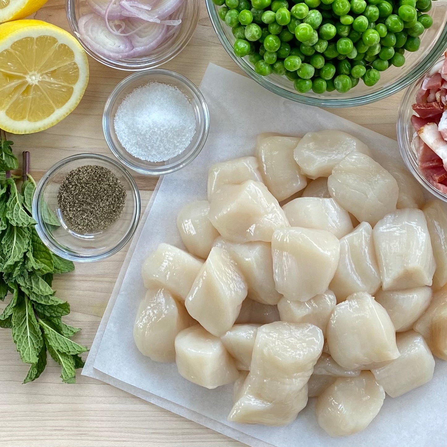 Raw wild Alaska weathervane scallops on a plate with lemon and herbs