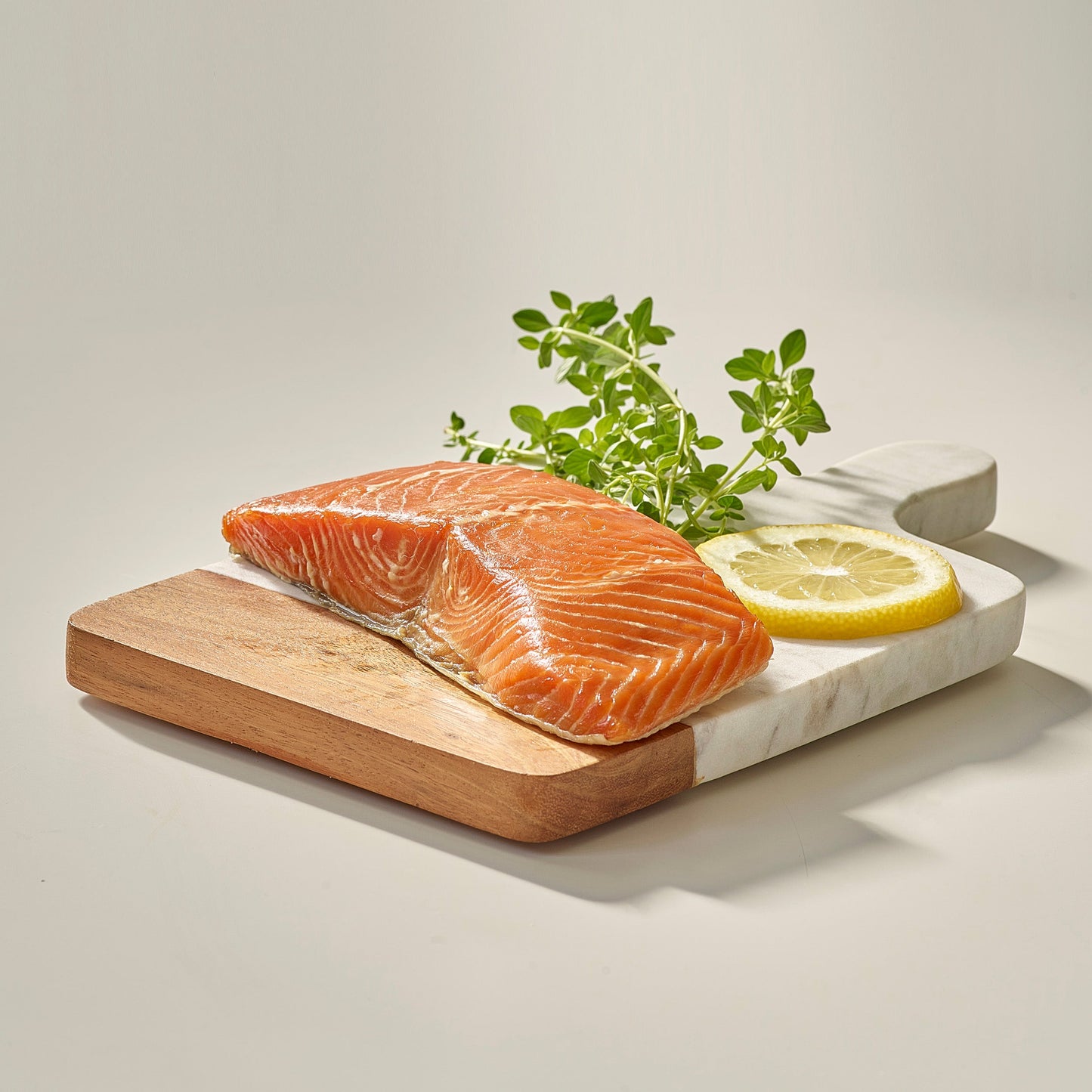 Wild Alaskan smoked king salmon fillet on a wooden board with lemon and fresh herbs.