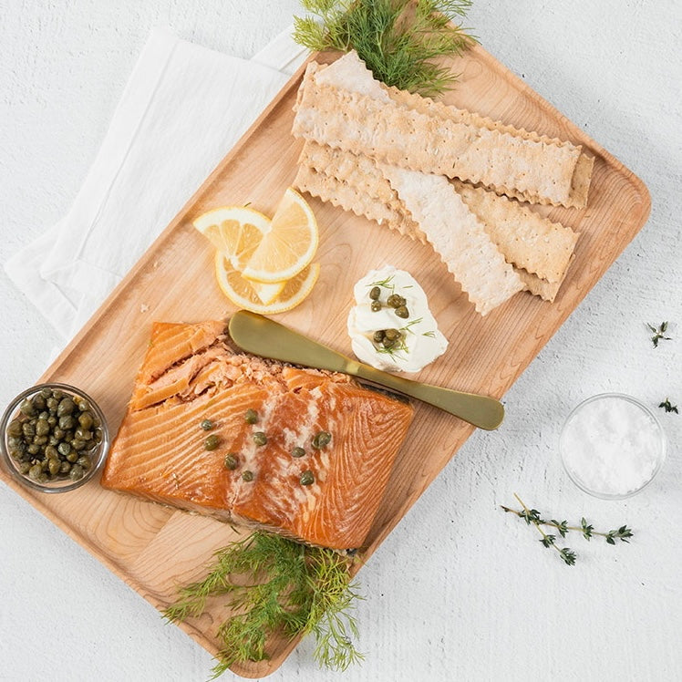 Wild Alaskan king salmon with cream cheese, capers and crackers on a cutting board.