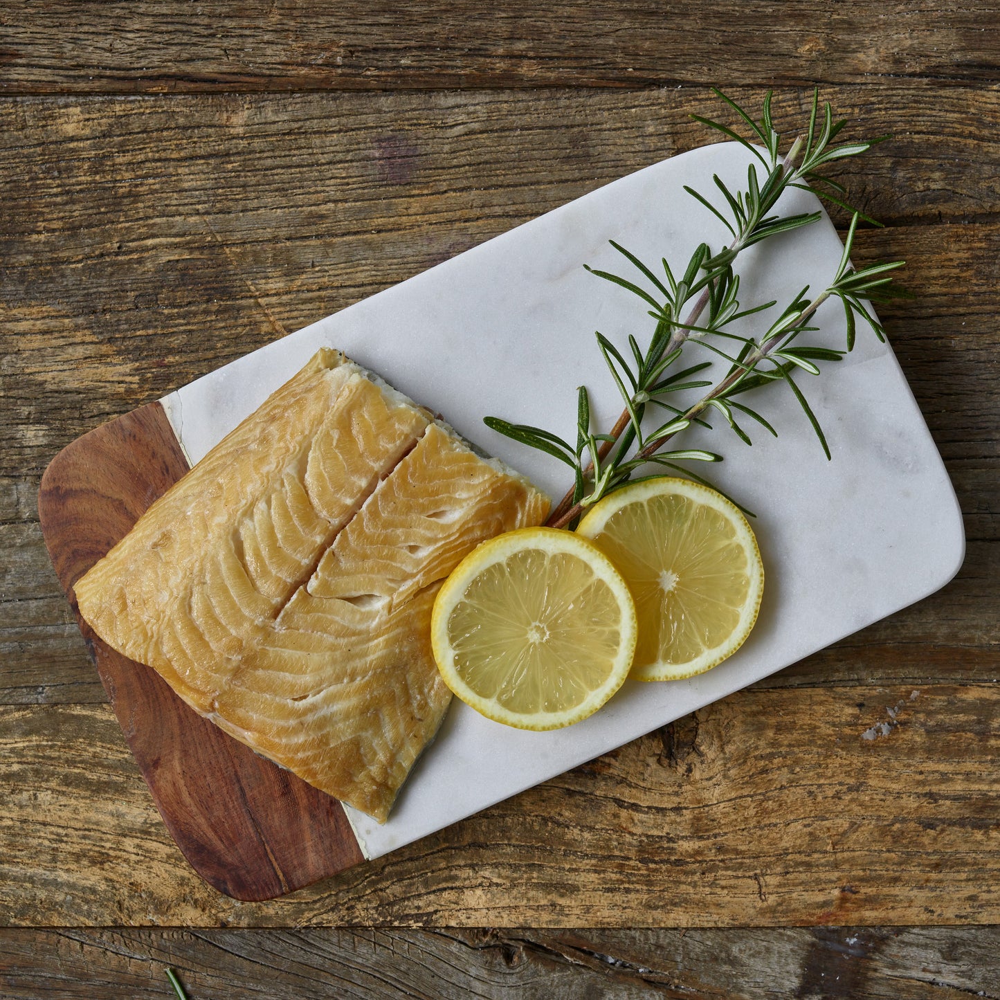 Wild Alaska smoked sablefish fillet on a cutting board with lemon slices and rosemary