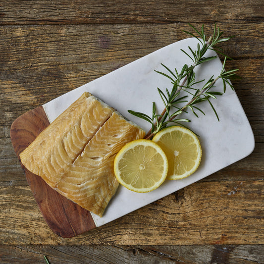 Wild Alaska smoked sablefish fillet on a cutting board with lemon slices and rosemary