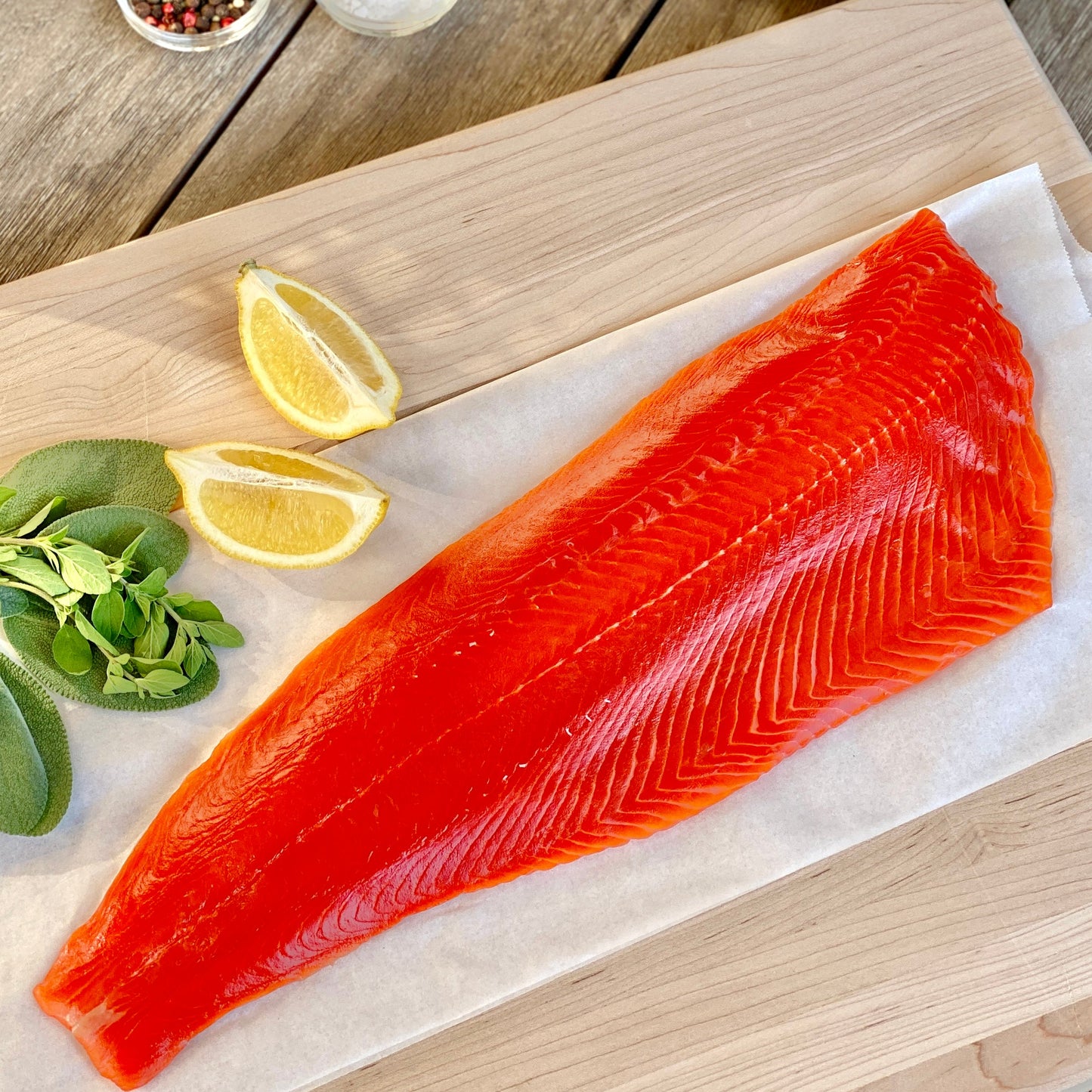 Wild Alaskan sockeye salmon fillet on a cutting board with lemon and herbs.