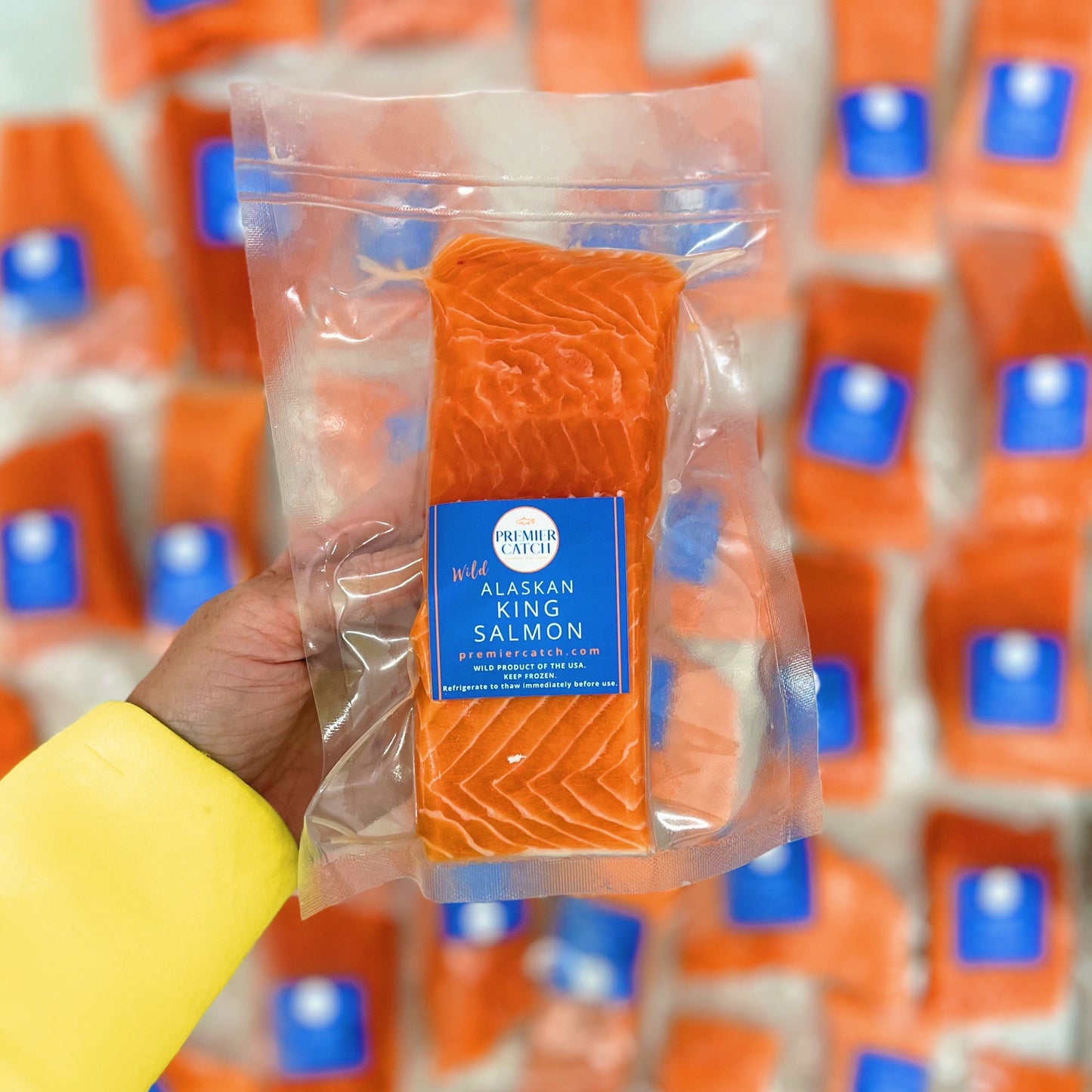 Packaged wild king salmon fillet held by a hand with a blurred background of similar packaging.