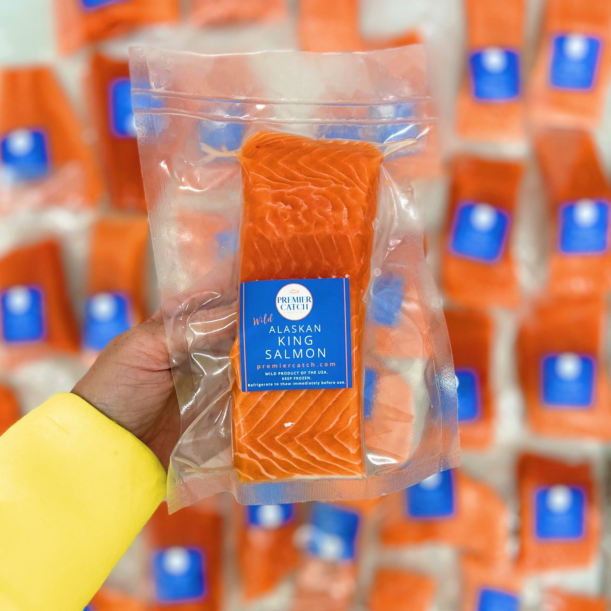 Packaged wild king salmon fillet held by a hand with a blurred background of similar packaging.