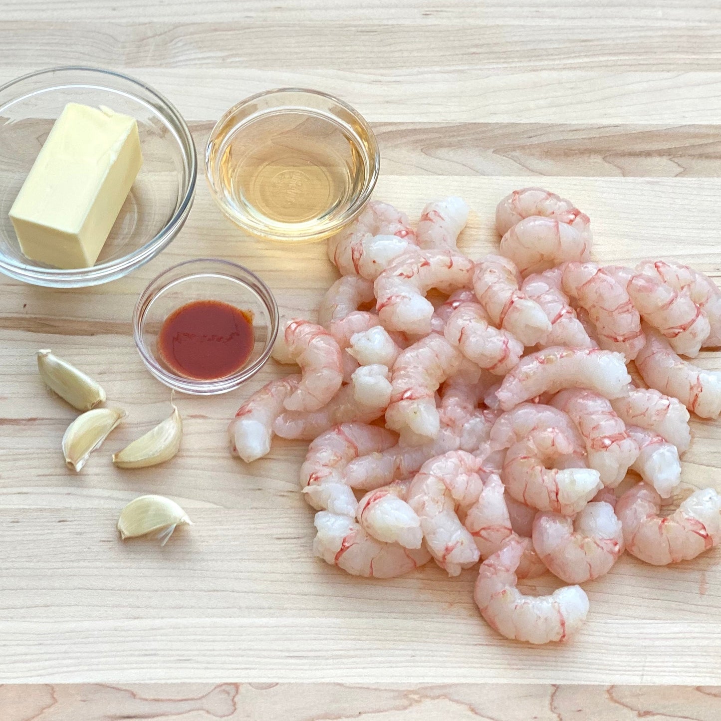 Raw wild alaskan spot prawns with butter, garlic, and oil on a wooden surface