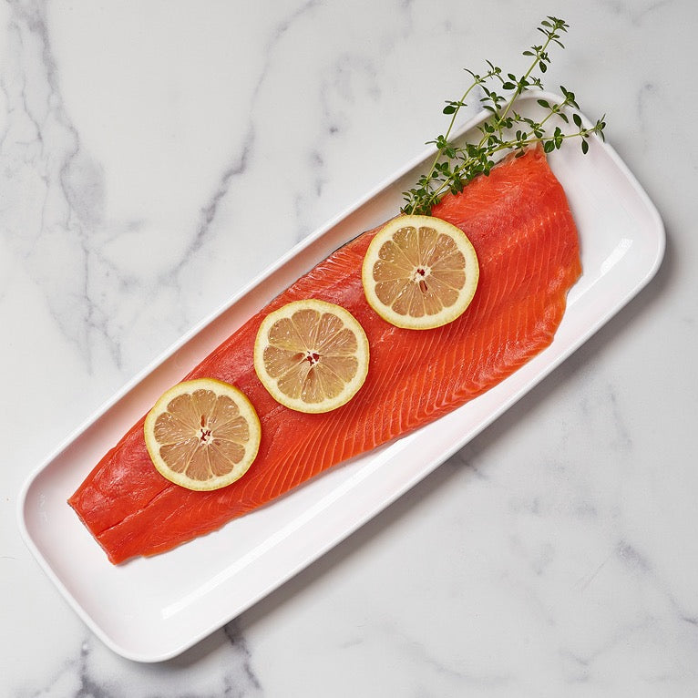 Wild Alaskan sockeye salmon fillet with lemon slices on a white plate.