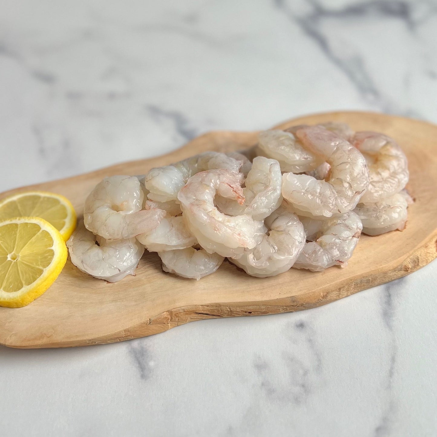 Raw wild Gulf shrimp arranged on a wooden board with lemon slices on a marble background