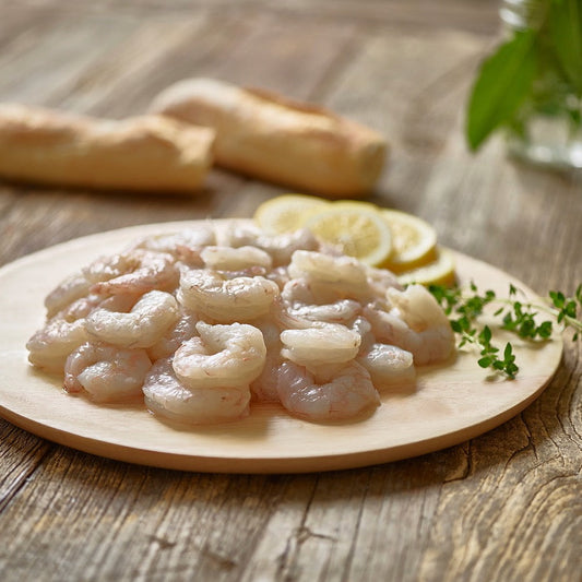 Raw wild Gulf shrimp on a wooden plate with lemon slices on a rustic wooden table